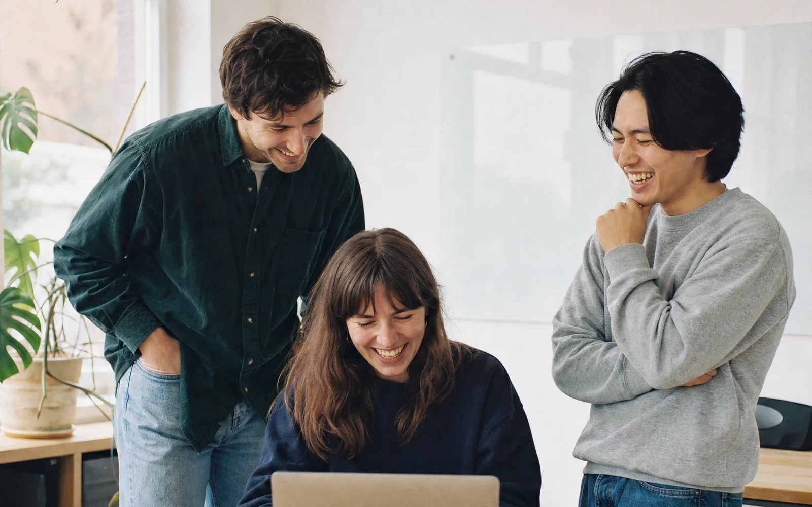 Drei Mitarbeitende von Songbotschaft lachen gemeinsam über etwas auf einem Laptop